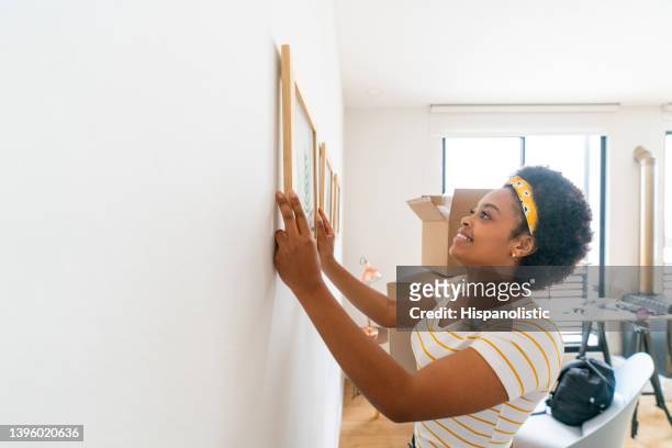 woman moving house and hanging a painting on the wall - hanging picture frame stock pictures, royalty-free photos & images