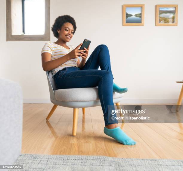 mujer feliz relajándose en casa y enviando mensajes de texto en su teléfono celular - cuarentena fotografías e imágenes de stock