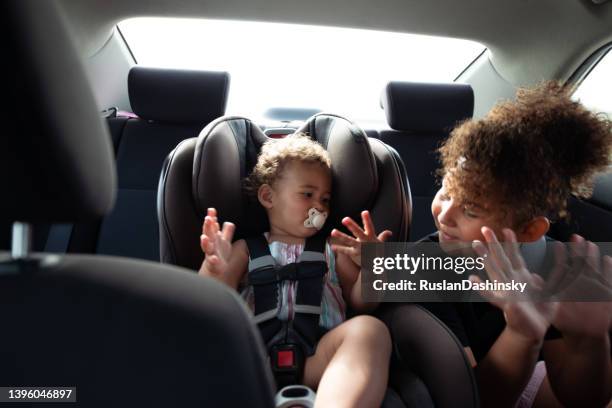 happy sisters showing fingers, playing in the back seat of the car. - baby accessories the dummy stock pictures, royalty-free photos & images