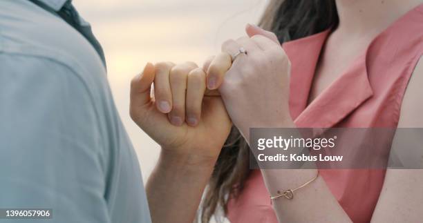 an unrecognizable couple holding hands and wearing an engagement ring. closeup of a man and woman after their proposal at the beach - oath 個照片及圖片檔