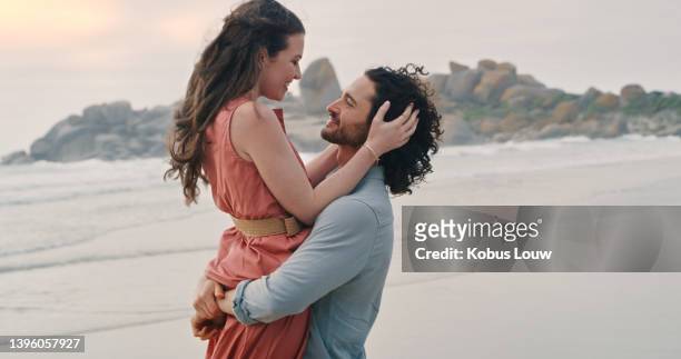 a happy young couple on the beach. carefree man and woman in love, hugging and embracing at the seaside - carefree moment stock pictures, royalty-free photos & images