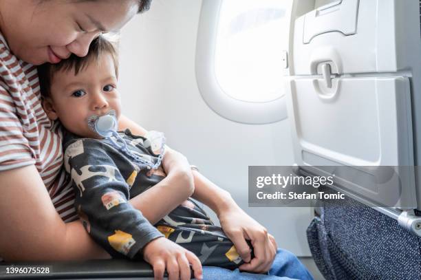 mother taking airplane with a baby boy. baby traveling in airplane flying sitting on his mother lap in the aircraft - baby accessories the dummy stock pictures, royalty-free photos & images