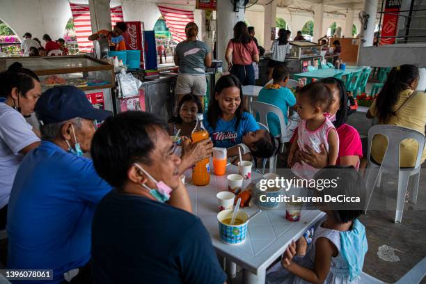 Families eat dinner around the corner from presidential candidate Ferdinand "Bongbong" Marcos polling station on the evening before election day on...