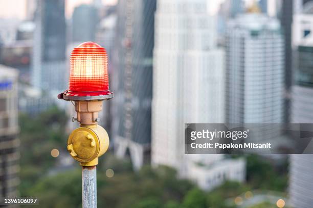 red lamp of obstacles installed on the roof of high-rise buildings to ensure flight safety and warning of dangers for planes on a red warning light city view background. - luchtaanval stockfoto's en -beelden