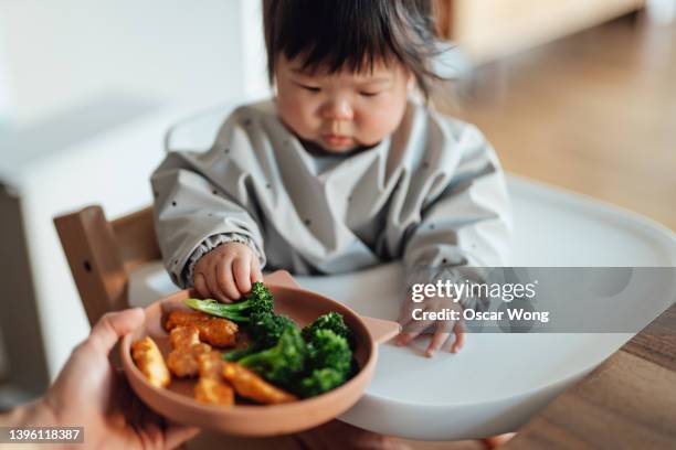 baby girl learning to feed herself with finger foods - panierter fisch stock-fotos und bilder