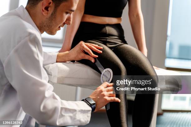 physical therapists examining young woman on treatment table, using goniometer to measure range of motion of knee. - human knee stock pictures, royalty-free photos & images