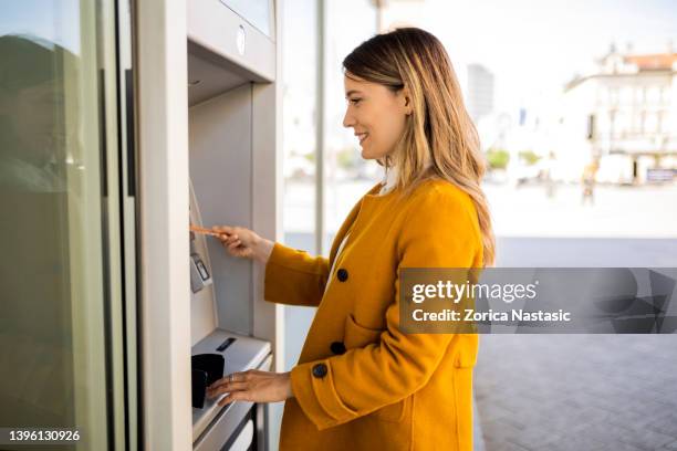 young woman at the atm - atm cash stock pictures, royalty-free photos & images