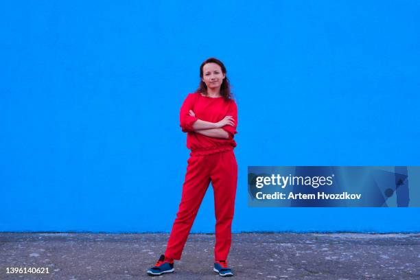 woman dressed in red casual style costume, holding her hands on chest. vibrant blue wall background - woman smiling white background stock-fotos und bilder