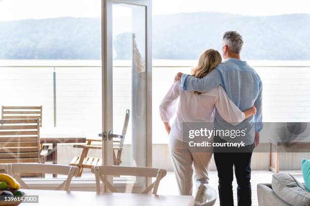 mature couple looking at the view in their waterfront home - balcony window stock pictures, royalty-free photos & images