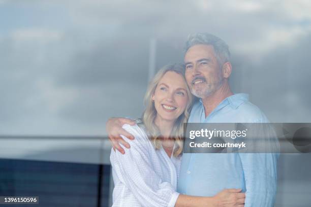 mature couple looking at the view in their home. they look happy and contented. - window view stockfoto's en -beelden