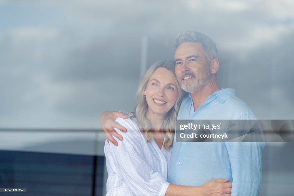 Mature couple looking at the view in their home. They look happy and contented.