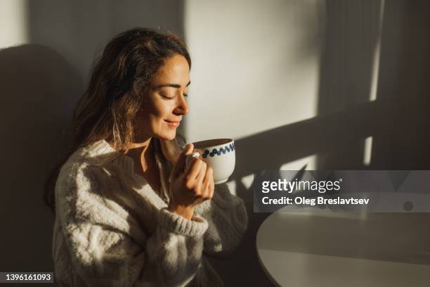 young pretty woman enjoying morning coffee at home. beautiful sun light in kitchen room. - tee stock-fotos und bilder