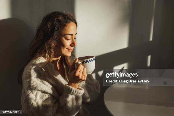 young pretty woman enjoying morning coffee at home. beautiful sun light in kitchen room. - woman relaxation stock pictures, royalty-free photos & images