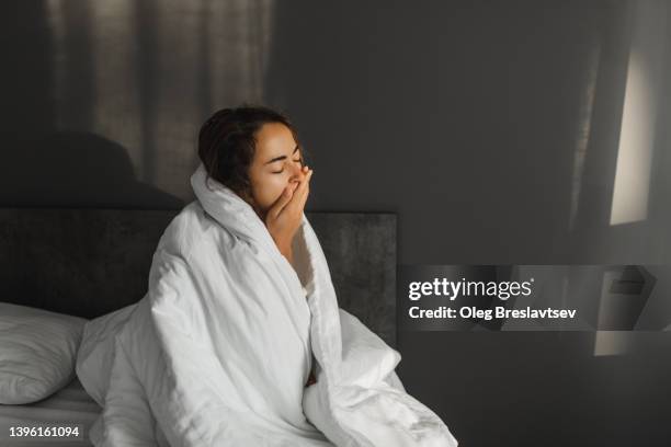 woman yawning and can't wake up in morning. sitting in bed covered with blanket. - gähnen stock-fotos und bilder