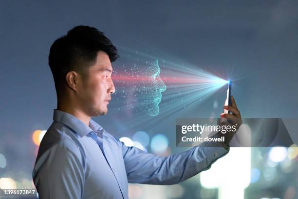 young chinese businessman using mobile phone with facial recognition at night - facial recognition technology stock-fotos und bilder