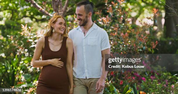 une jeune femme enceinte marchant dans la nature avec son mari, partageant un moment romantique. couple heureux profitant d’un congé de maternité relaxant à l’extérieur - femme enceinte jardin photos et images de collection