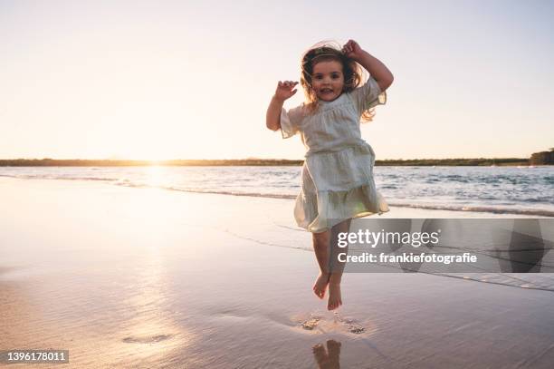 ein kleines mädchen, das in die luft springt - girl blowing sand stock-fotos und bilder