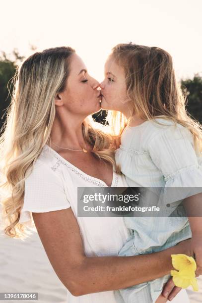 madre besando a su hija al atardecer - mothers day beach fotografías e imágenes de stock