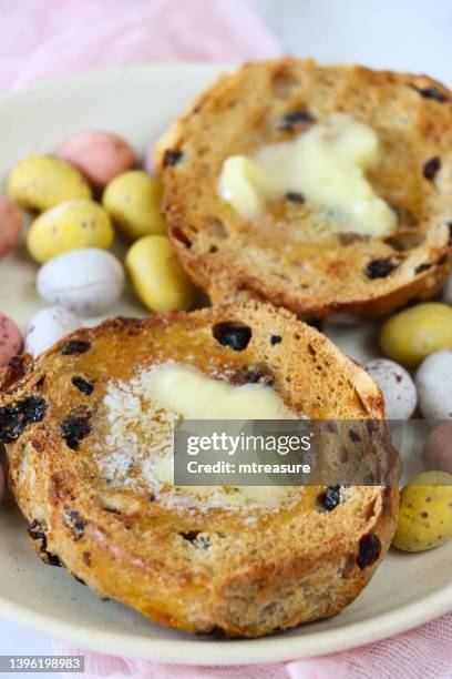 close-up image of toasted, easter hot cross bun with melted butter on plate with chocolate mini eggs, pink muslin, marble effect background, elevated view, focus on foreground - raisin toast stock pictures, royalty-free photos & images