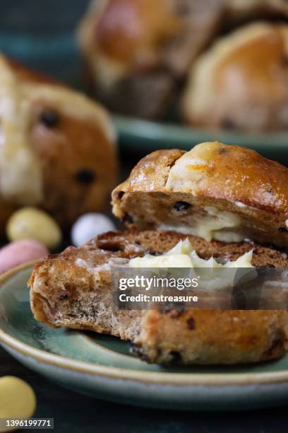 close-up image of buttered, toasted, easter hot cross bun with missing bite on plate, chocolate mini eggs, wood grain background, focus on foreground - raisin toast stock pictures, royalty-free photos & images