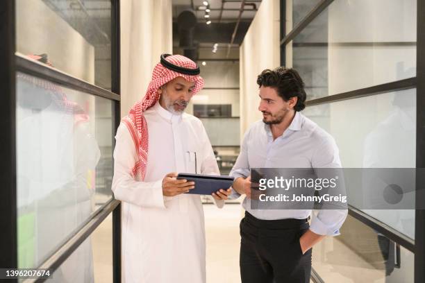 saudische geschäftsleute in den 30er und 40er jahren, die sich im büroflur unterhalten - saudiarabien stock-fotos und bilder