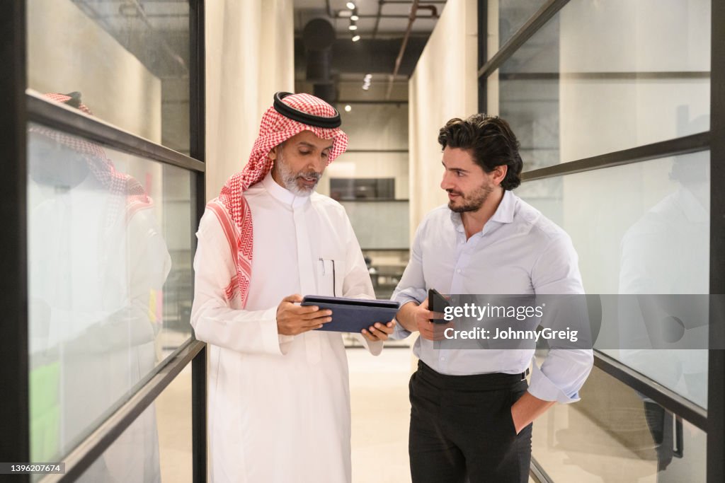 Saudi businessmen in 30s and 40s talking in office hallway