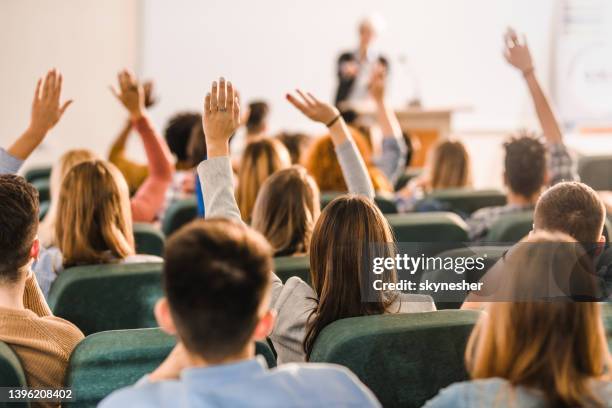 rear view of large group of students raising arms during a class at amphitheater. - college classroom stock pictures, royalty-free photos & images