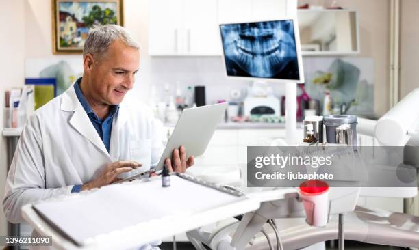 médecin dentiste assis au bureau avec un ordinateur portable - dentiste photos et images de collection