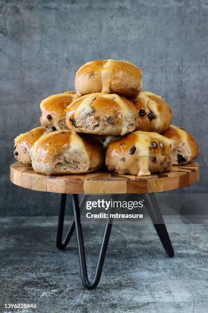 image of freshly baked, homemade easter hot cross buns piled on cake stand, mottled grey background, home baking concept, focus on foreground - hot cross bun stock pictures, royalty-free photos & images