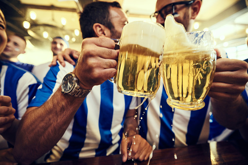 Close up of male sports fans toasting with beer in a pub.