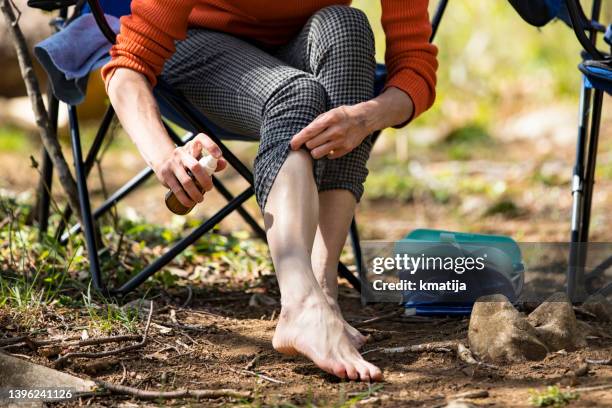 mid adult woman spraying her legs with insect repellant while sitting in nature - mug stockfoto's en -beelden