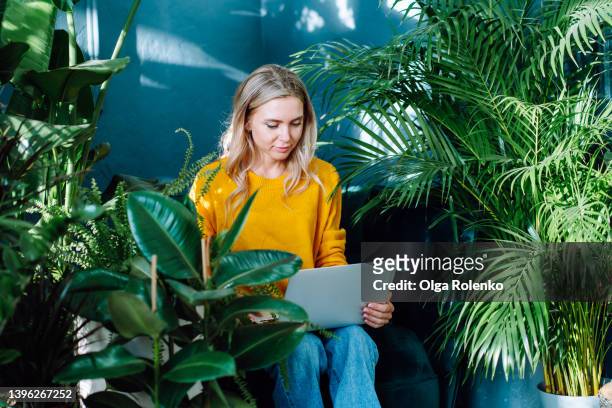 confident and professional blond businesswoman working online on laptop at her greenhouse workplace at flower shop - circondare foto e immagini stock