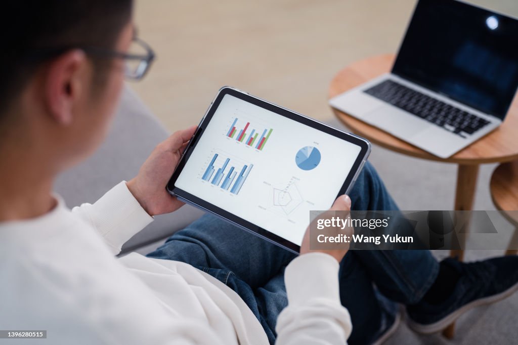 Back view of young man using tablet to check chart data
