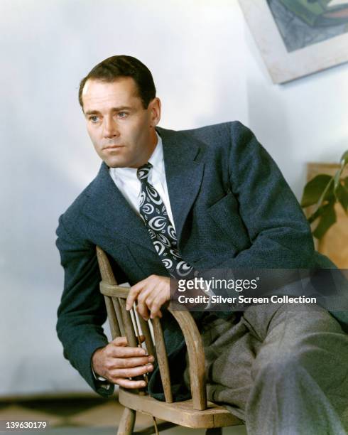 Henry Fonda , US actor, wearing a grey jacket, white shirt and a patterned tie while sitting on a chair in a studio portrait, circa 1945.