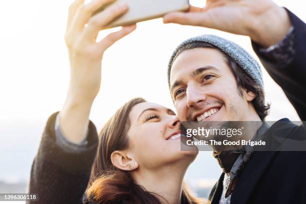 close up shot of young couple taking selfie against clear sky in winter - coppia eterosessuale foto e immagini stock
