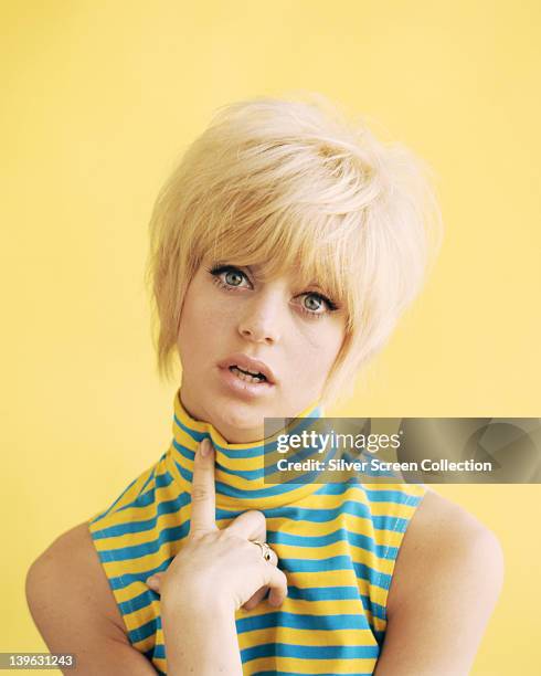 Goldie Hawn, US actress, wearing a blue and yellow striped sleeveless top in a studio portrait, against a yellow background, circa 1965.