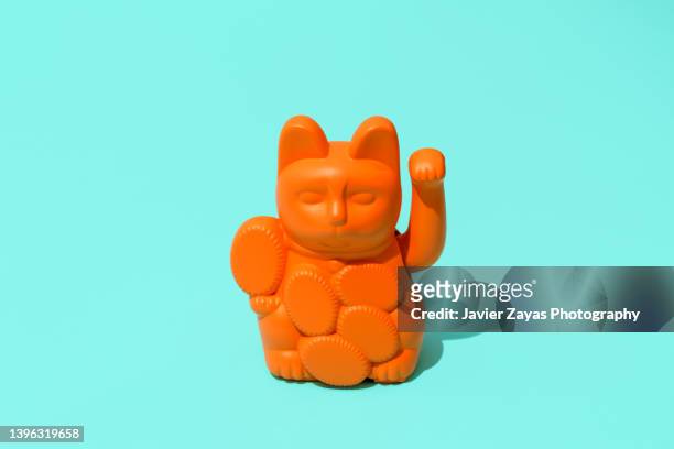 orange lucky cat (maneki neko) against green background - daruma stock pictures, royalty-free photos & images