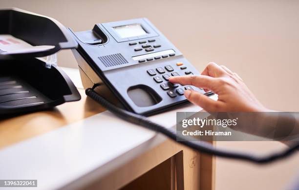 closeup of a woman making a call on a telephone in an office alone. one female only dialling a phone number with her fingers on a keypad at a receptionist's front desk. administrator and secretary consulting and transferring calls from a help desk - land line phone stock pictures, royalty-free photos & images