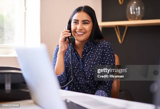 joven empresaria india hablando por teléfono en una oficina sola. una mujer solo hace una llamada mientras trabaja como recepcionista en una recepción. administrador y secretaria consultando y transfiriendo llamadas desde una mesa de ayuda en un centro d - teléfono con cable fotografías e imágenes de stock