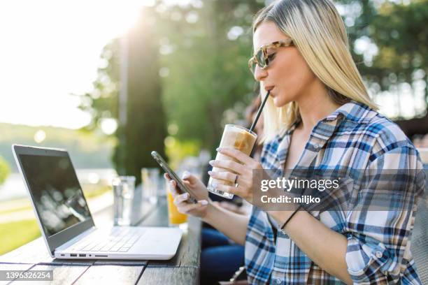 mujer joven relajándose pero trabajando en una computadora portátil en una cafetería - café frappé fotografías e imágenes de stock