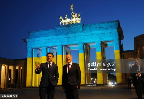 German Chancellor Olaf Scholz and French President Emmanuel Macron stand in front of the Brandenburg Gate that is illuminated in the colors of the...