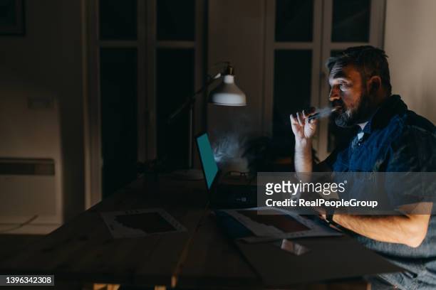 freelancer lifestyle. remote job. virtual office. mature man working online using laptop in modern room - vape cigarette stock pictures, royalty-free photos & images