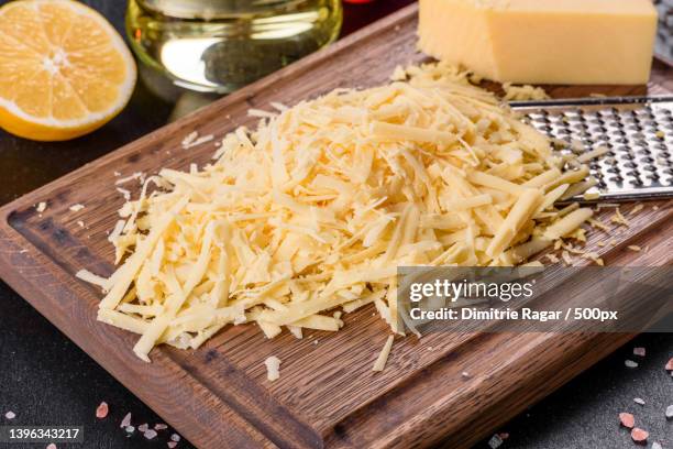 fresh hard cheese grated on a large grater on a wooden cutting board - cheese stockfoto's en -beelden