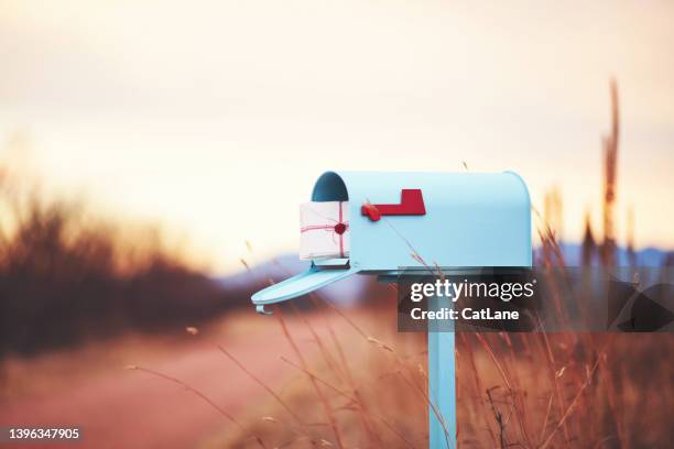 teal mailbox filled with a stack of love letters on a rural path at dusk - love letter mailbox stock pictures, royalty-free photos & images