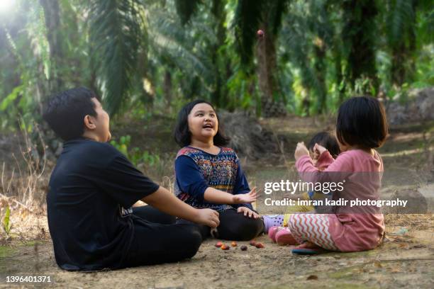 asian sibling playing batu seremban at the oil palm plantation - malaysia batik stock pictures, royalty-free photos & images
