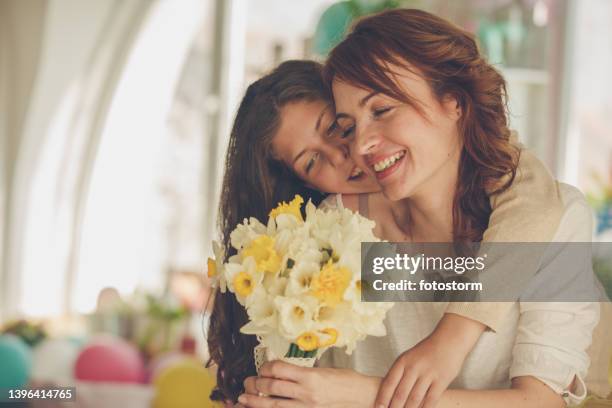 cheerful woman getting a bouquet of yellow daffodils from her daughter for mother's day - mothers day stock pictures, royalty-free photos & images