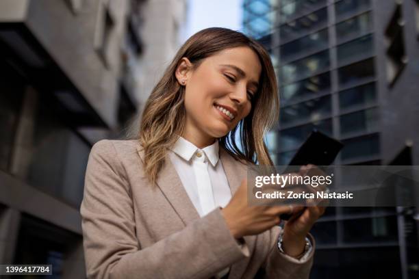 smiling young businesswoman standing alone using phone - 30 39 years stock pictures, royalty-free photos & images