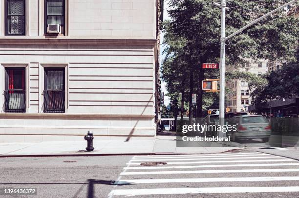 east 55 street corner in midtown manhattan at sunny midday, crosswalk red light, neo-classic architecture, cars blurred motion - corner city foto e immagini stock