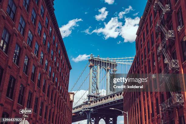 famous view of manhattan bridge against blue sky amidst brick walls industrial buildings of dumbo district, brooklyn, new york - manhattan bridge photos et images de collection