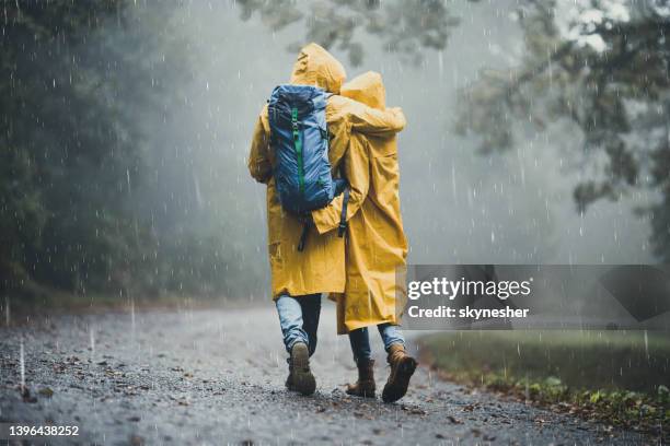 back view of embraced couple in raincoats hiking on a rain. - rain couple stockfoto's en -beelden